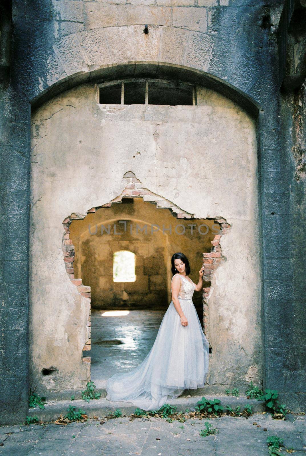 Bride stands near the dilapidated entrance of the old fortress. High quality photo