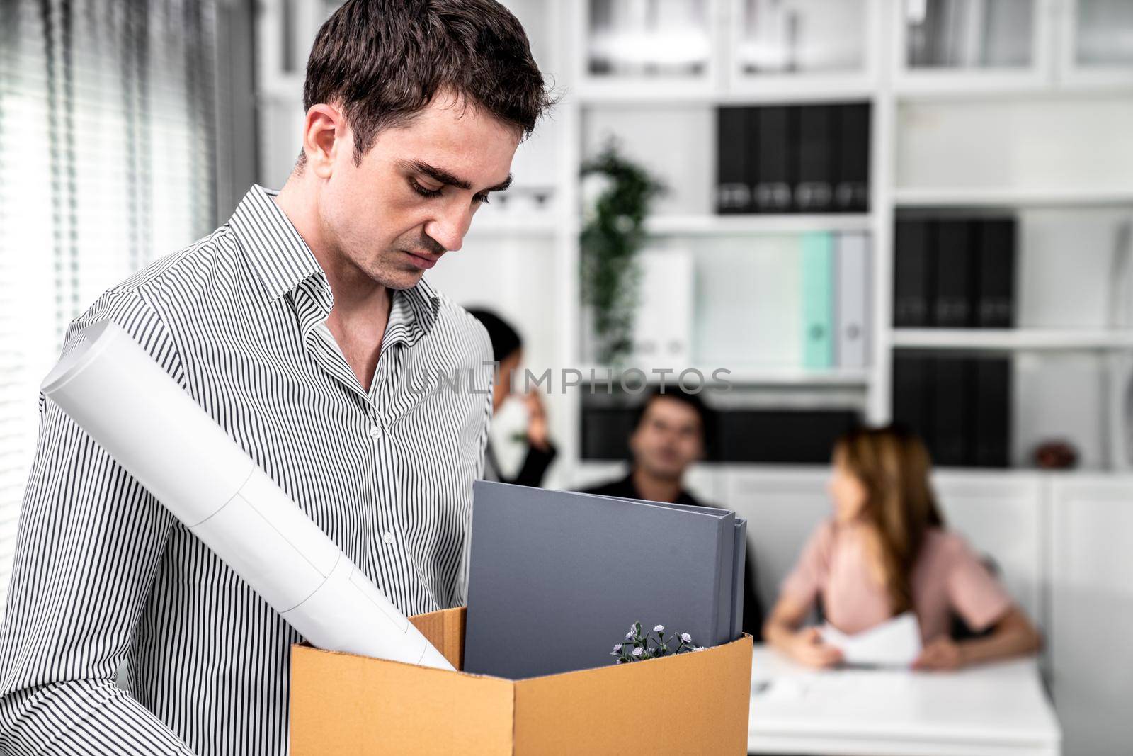 Depressed and disappointed employee packing his belongings after being fired for not being competent. Gossiped by his colleagues behind his back. Layoff due to economic depression.