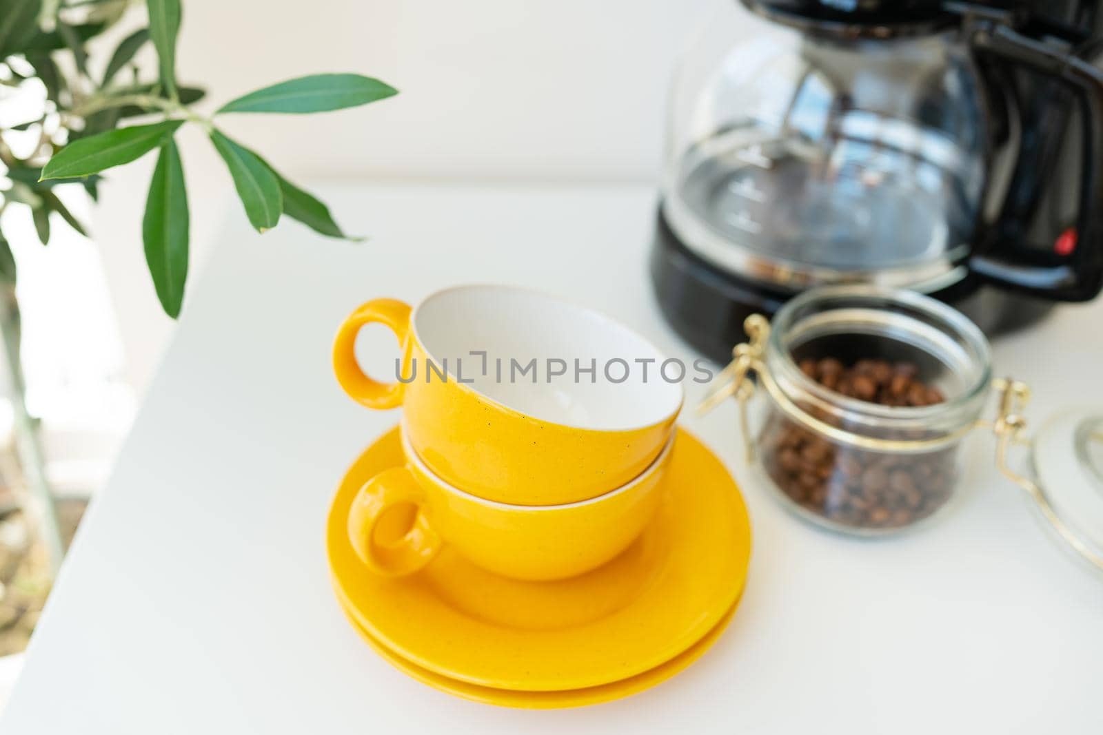 Beautiful morning, the process of making coffee. An automatic drip coffee maker stands with a yellow cup on a white table. Electric kitchen small household appliances