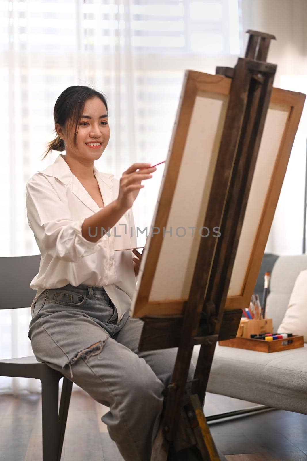 Pleasant millennial woman painting picture on canvas with oil paints in home studio. Leisure activity, creative hobby and art concept.