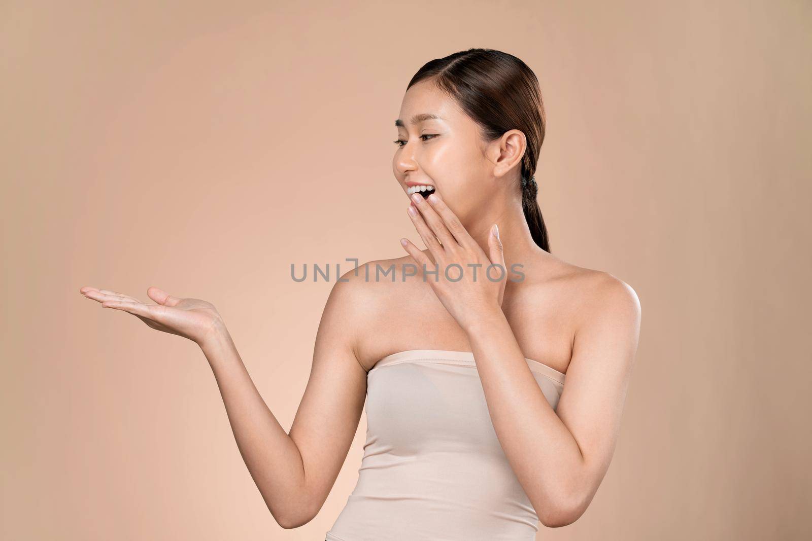 Portrait of ardent woman looking at camera, holding empty space for product, advertising text place, isolated background. Concept of healthcare advertising for skincare, beauty care product.