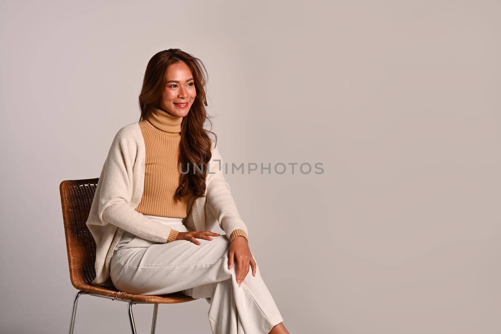 Gorgeous woman wearing stylish trendy clothes in earth tones sitting on beige background. Autumn and Winter concept.