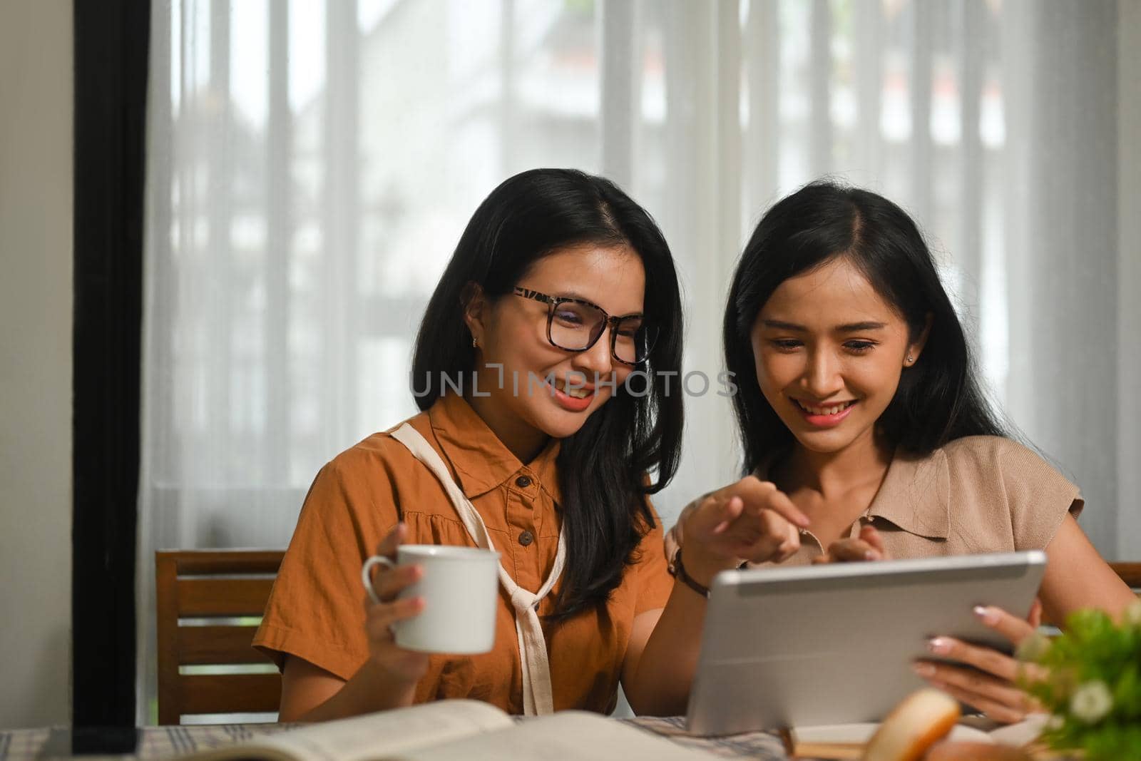 Two pretty young asian woman sitting in comfortable coffee shop and using digital tablet. People and technology concept.