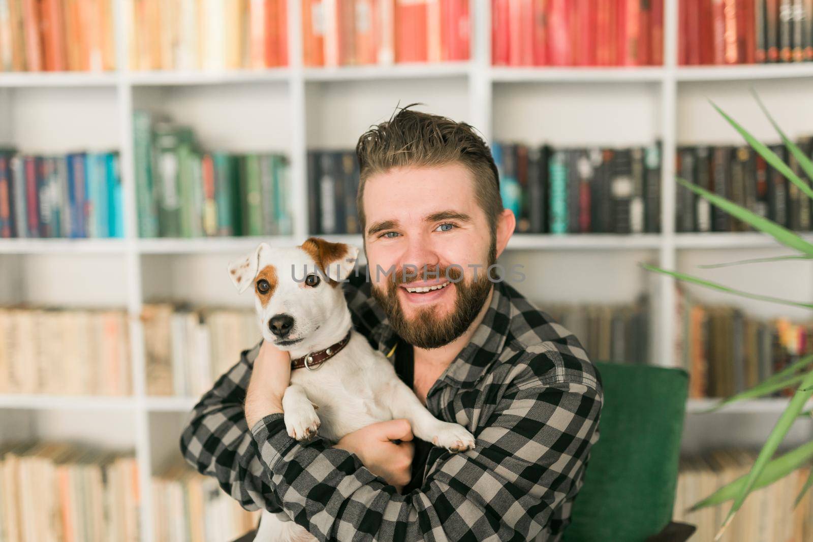 Happy male owner of jack russell terrier dog, feels responsibility of caring about pet, standing against bookshelves background. People and relationship with animals.