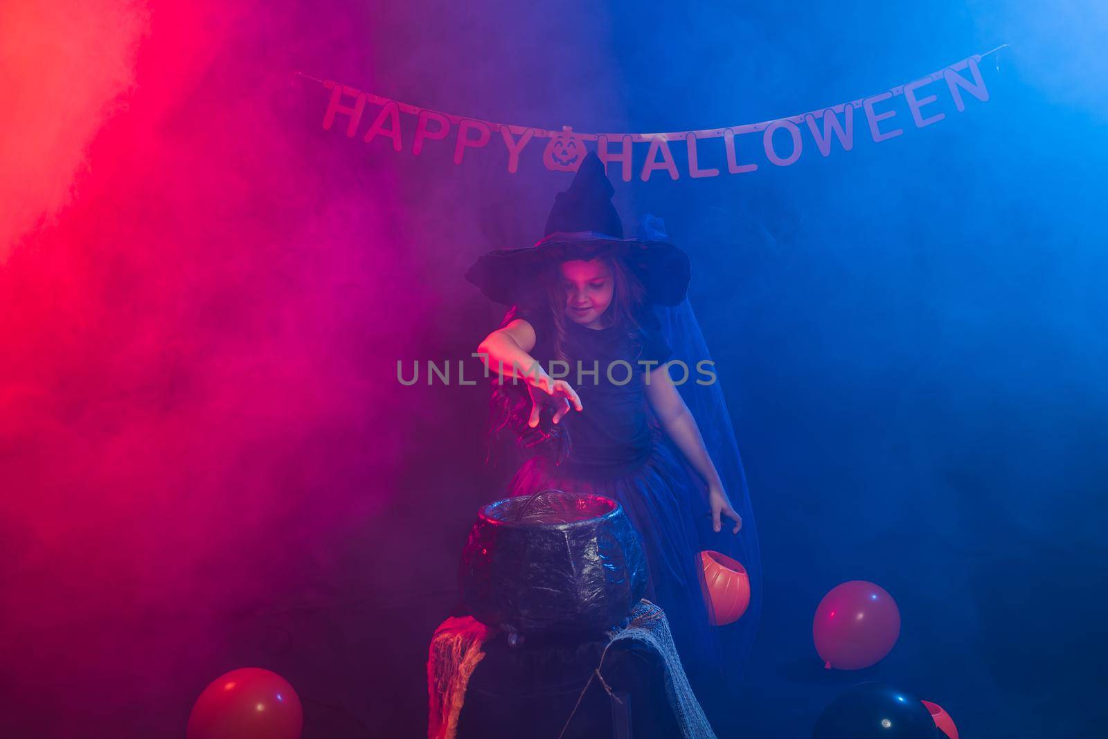 Child girl witch preparing a potion in the cauldron at halloween holidays