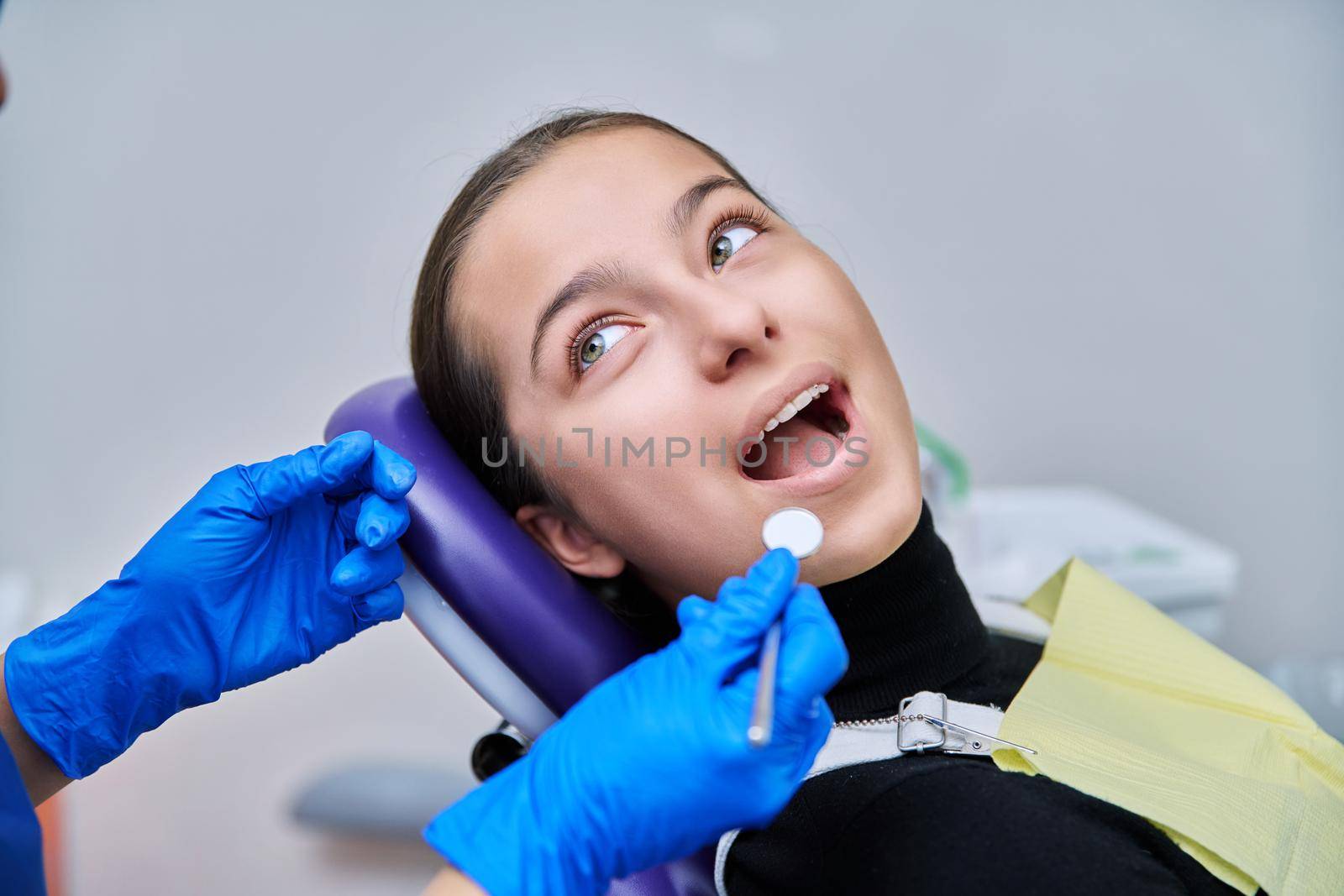 Young teenage female at dental checkup in clinic. Teenage girl sitting in chair, doctor dentist with tools examining patient's teeth. Adolescence, hygiene, dentistry, treatment, dental health care