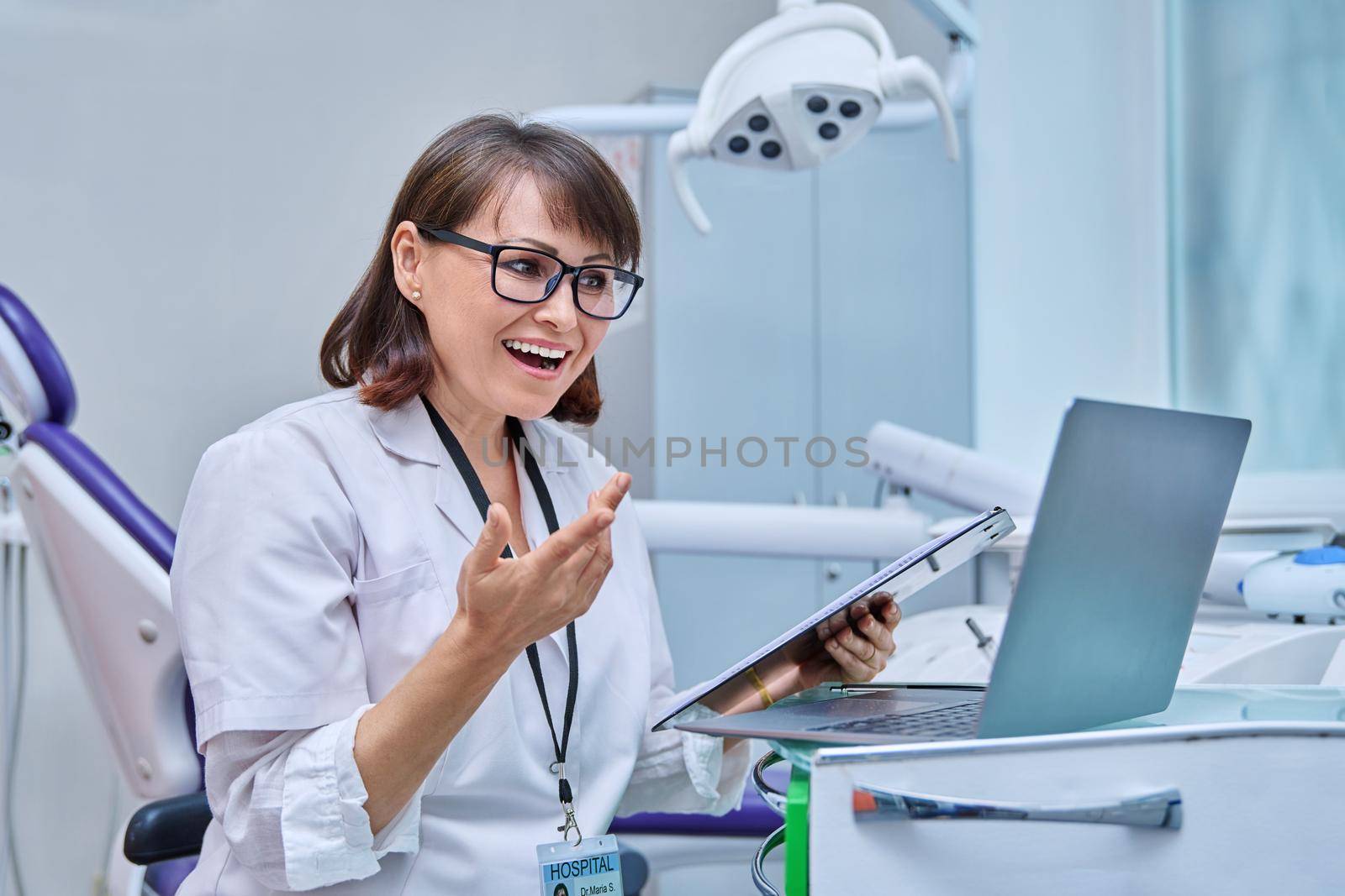 Doctor dentist working in office, using laptop clipboard, making video call conference, talking consulting patients online. Technology, medicine, dentistry, dental health care concept