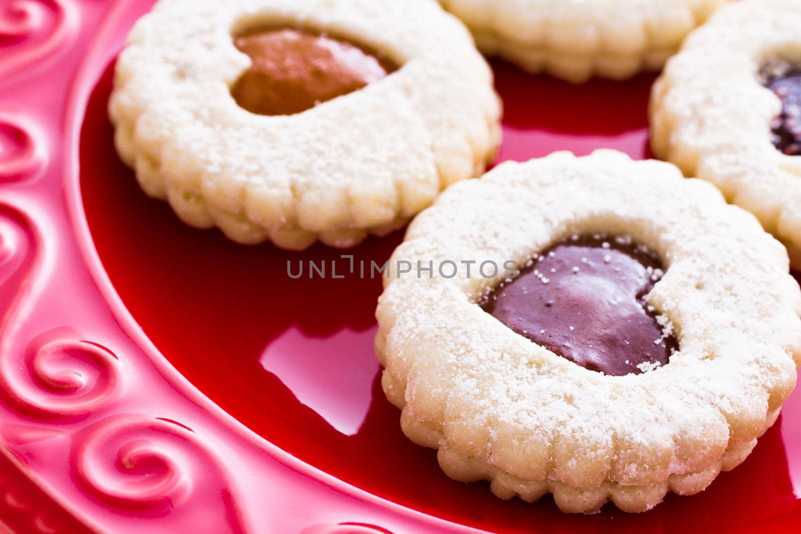 Linzer Torte cookies on red plate with powdered sugar sprinkled on top.
