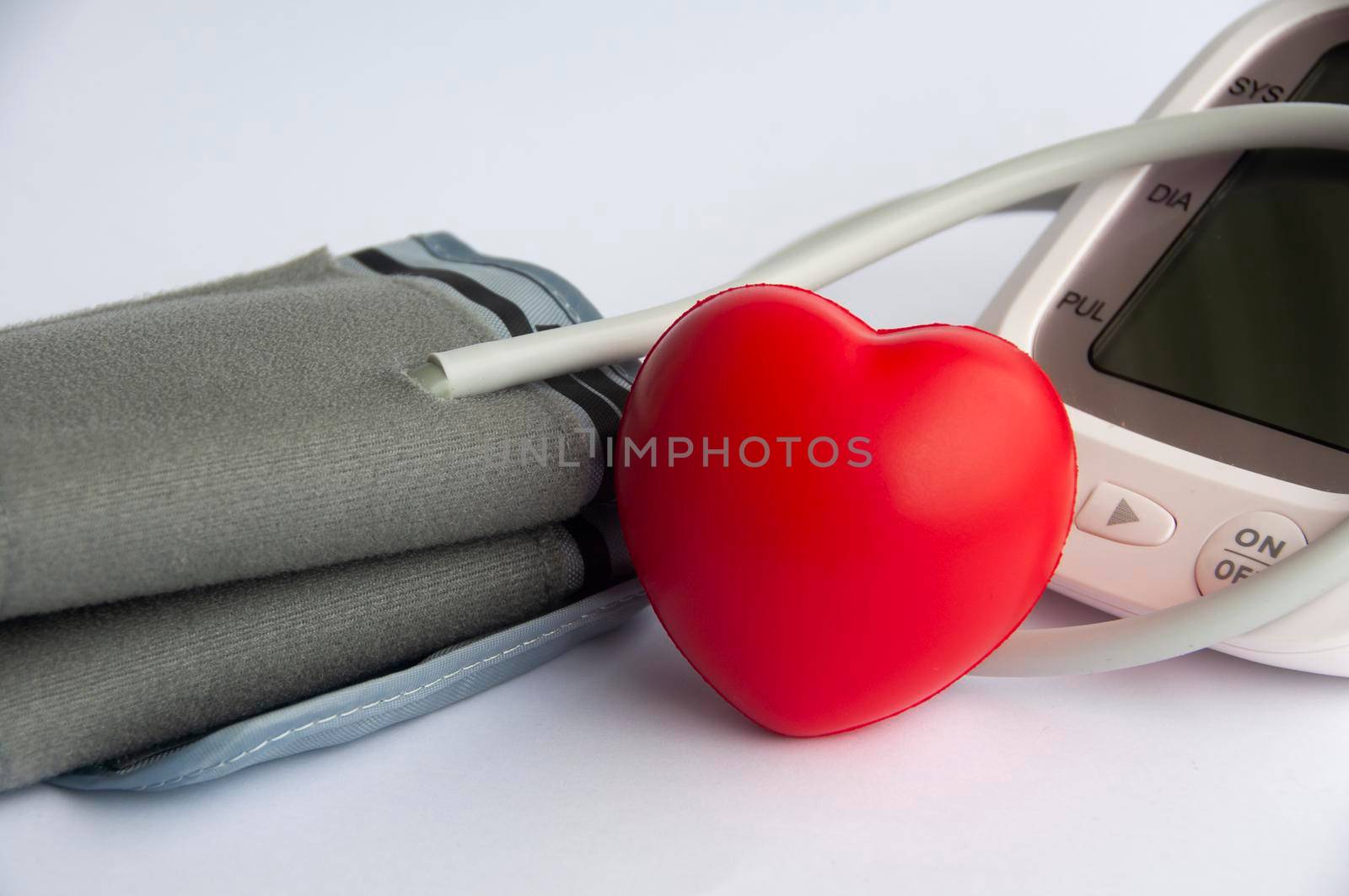 Digital blood pressure monitor and heart shape on white background.