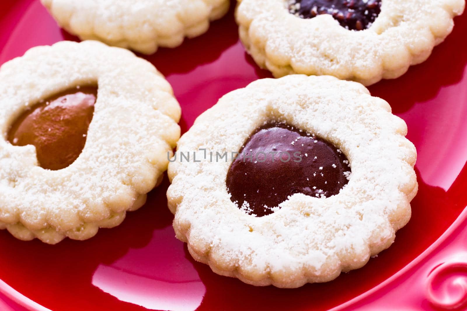 Linzer Torte cookies on red plate with powdered sugar sprinkled on top.