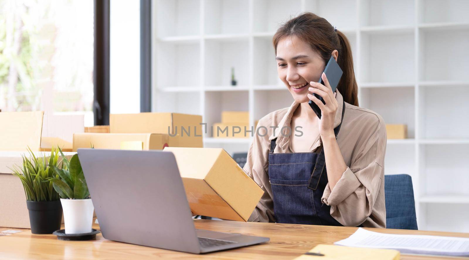 Startup small business entrepreneur or freelance Asian woman using a laptop with box, Young success Asian woman with her hand lift up, online marketing packaging box and delivery, SME concept. by wichayada