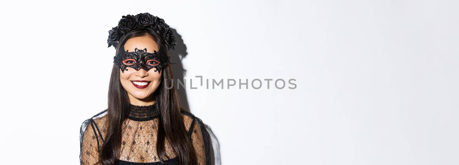 Close-up of mysterious woman in gothic wreath and black mask smiling at camera, celebrating halloween, standing over white background by Benzoix