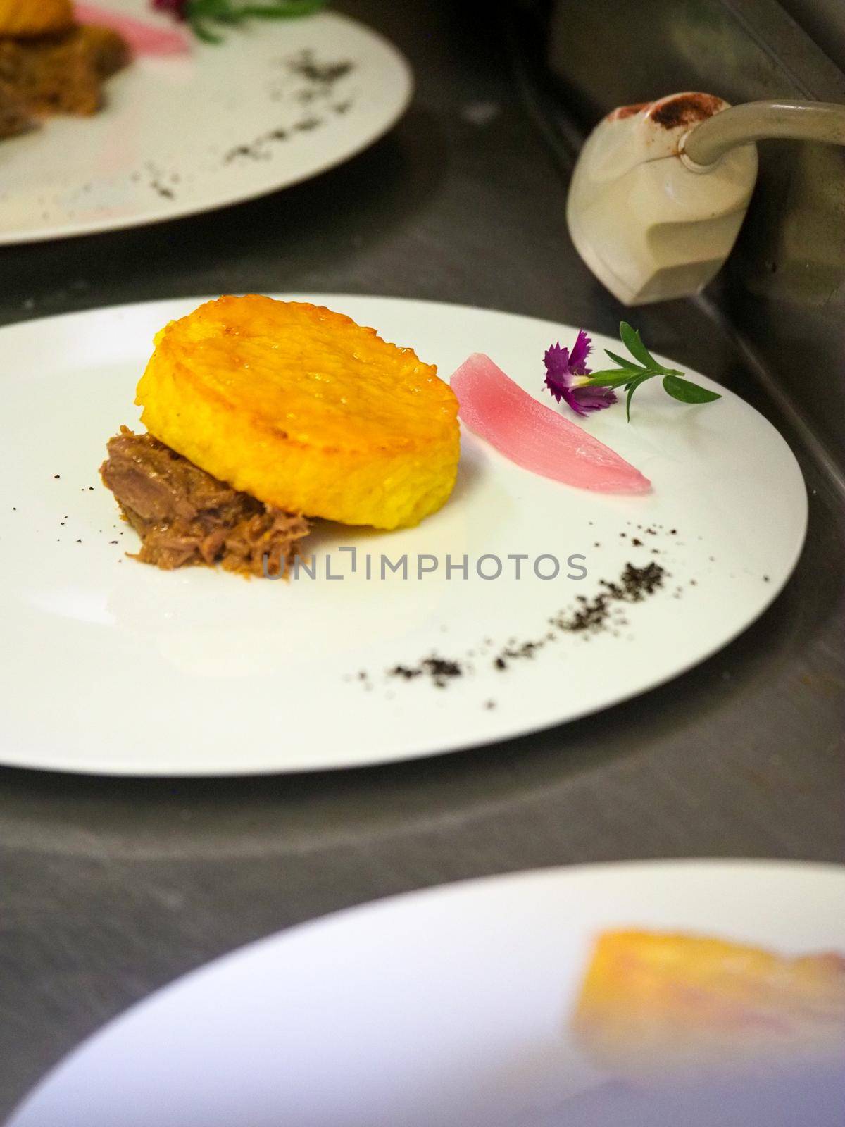 staff plating a modern second course meat decorated dish - line of prepared food for party