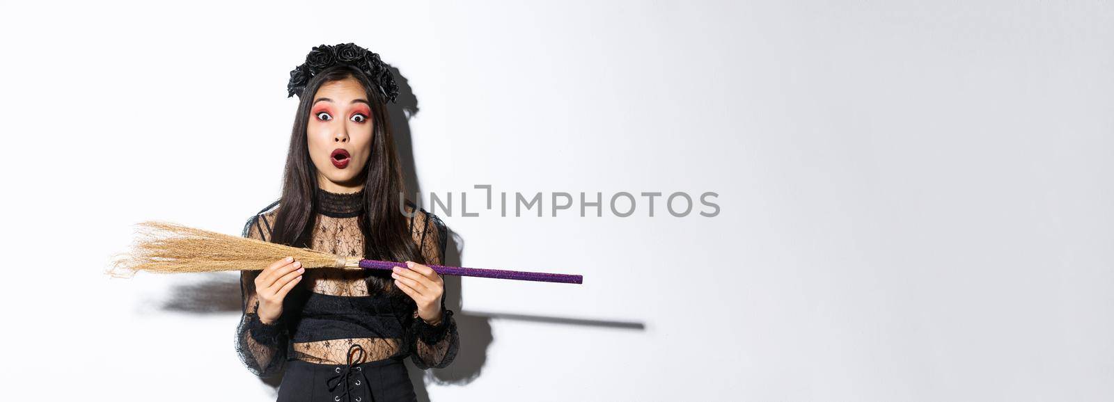 Image of surprised woman in halloween costume, holding witch broom and looking at camera amazed.