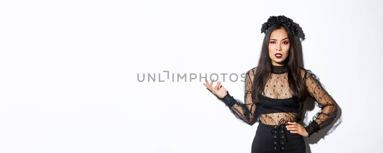 Angry and confused asian woman in witch costume looking bothered by annoying quetion, raising hand up and stare at camera pissed-off. Female at halloween party standing frustrated by Benzoix
