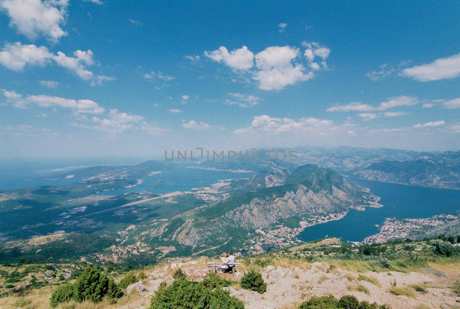 Bride and groom sit on a bench on the top of the mountain and look at the valley. High quality photo