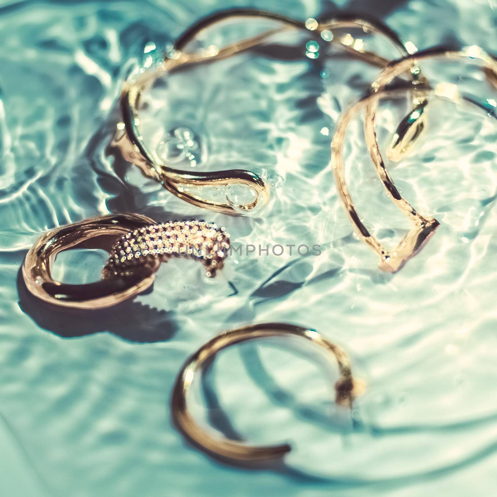 Golden bracelets, earrings, rings, jewelery on emerald water background, luxury glamour and holiday beauty design for jewelry brand ads by Anneleven