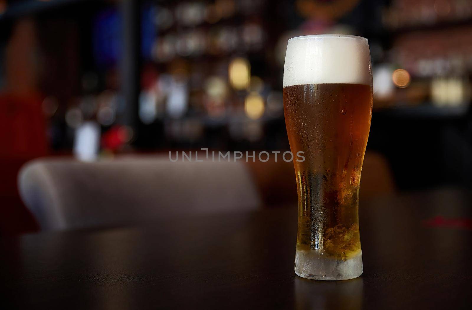 Fresh cold beer, glass of beer on a table in a bar on blurred bokeh background.