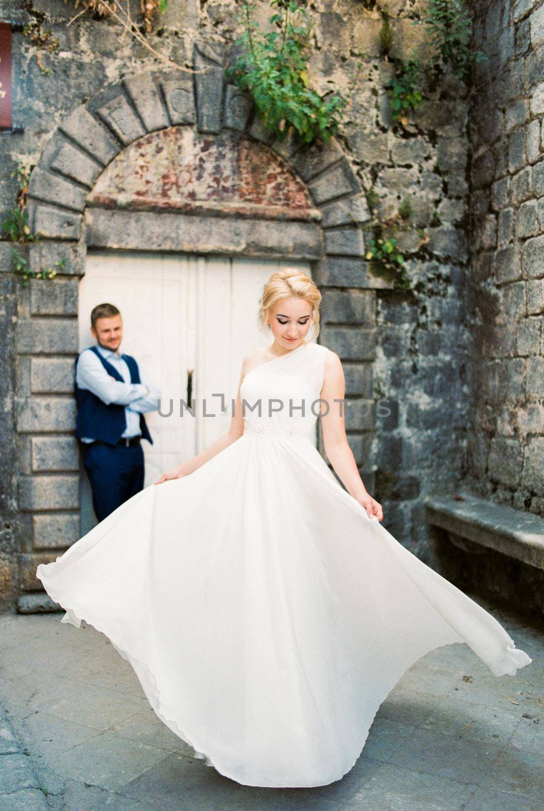 Bride in a white dress with fluttering floors stands in front of the groom. High quality photo