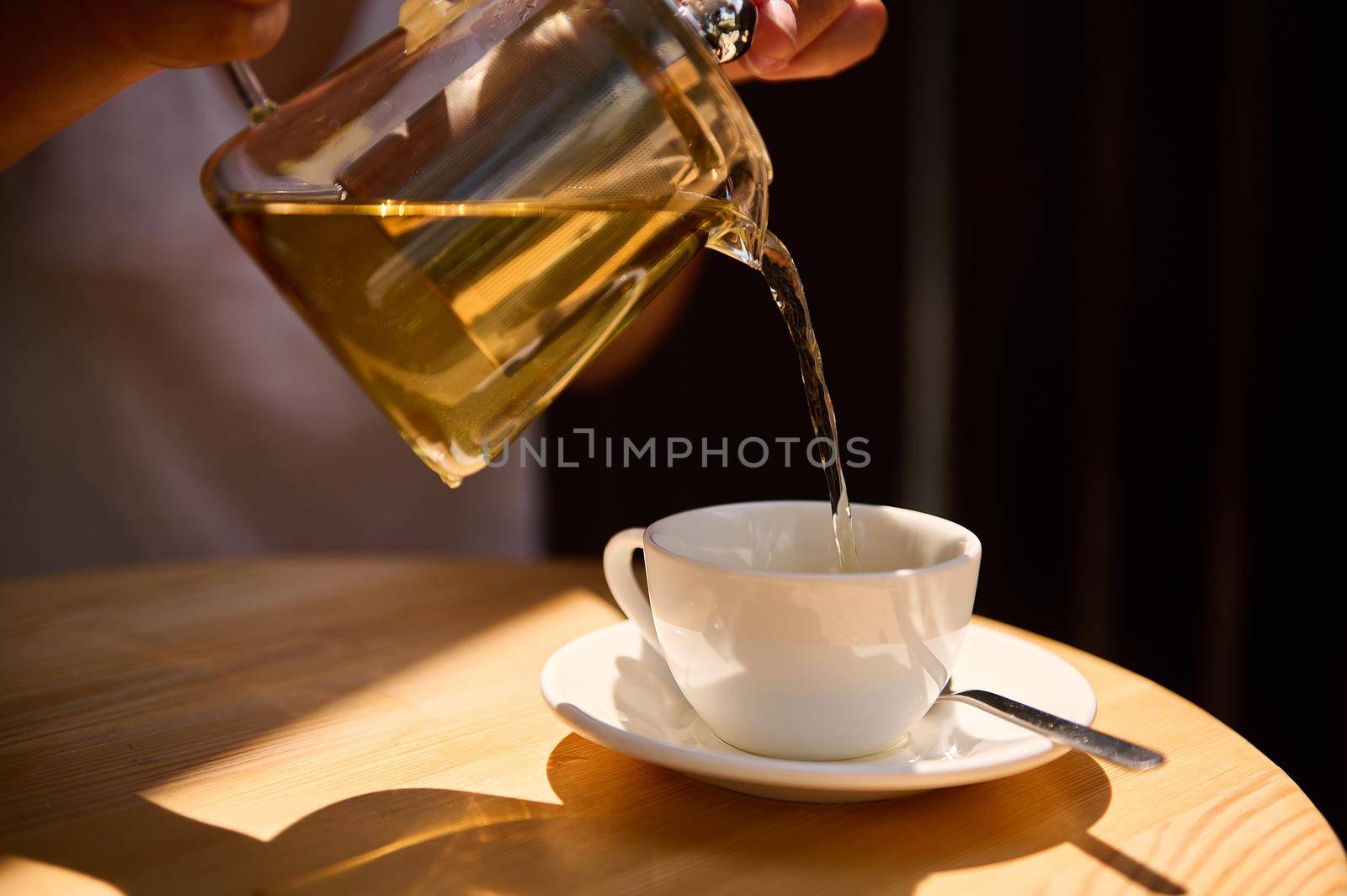 Close-up of pouring healthy antioxidant exotic green tea from glass teapot into a teacup by artgf