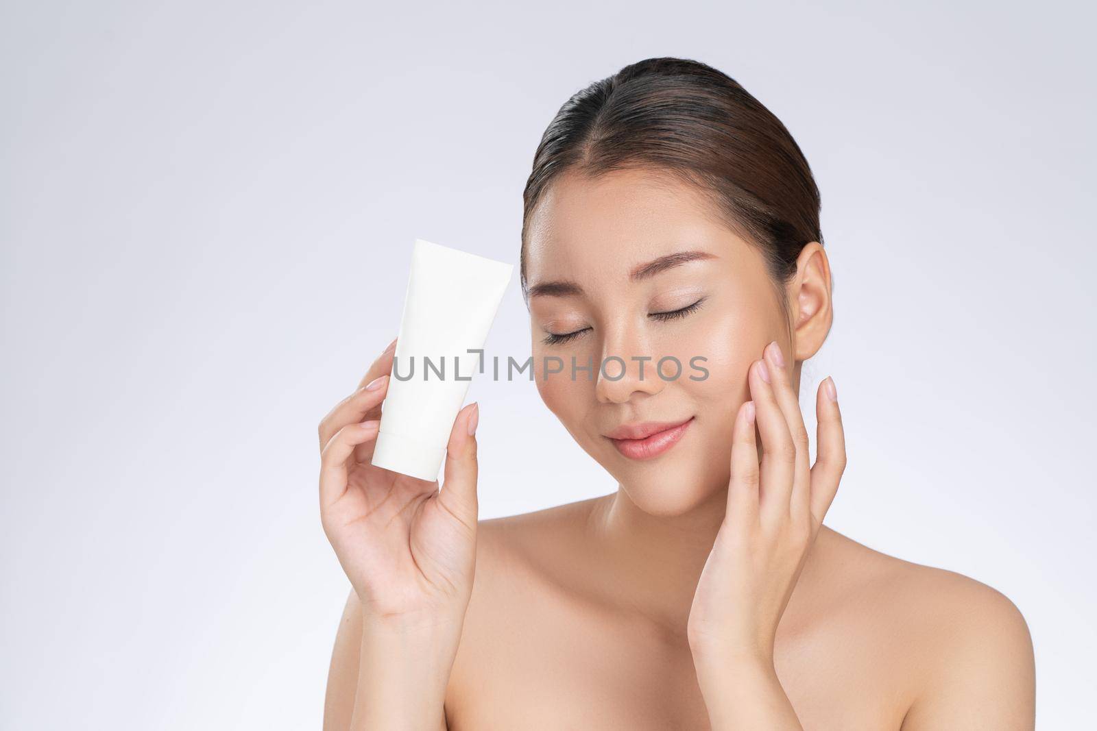 Gorgeous woman smiling holding mockup product for advertising text place, light grey background. Concept of healthcare for skin, beauty care product for advertising.