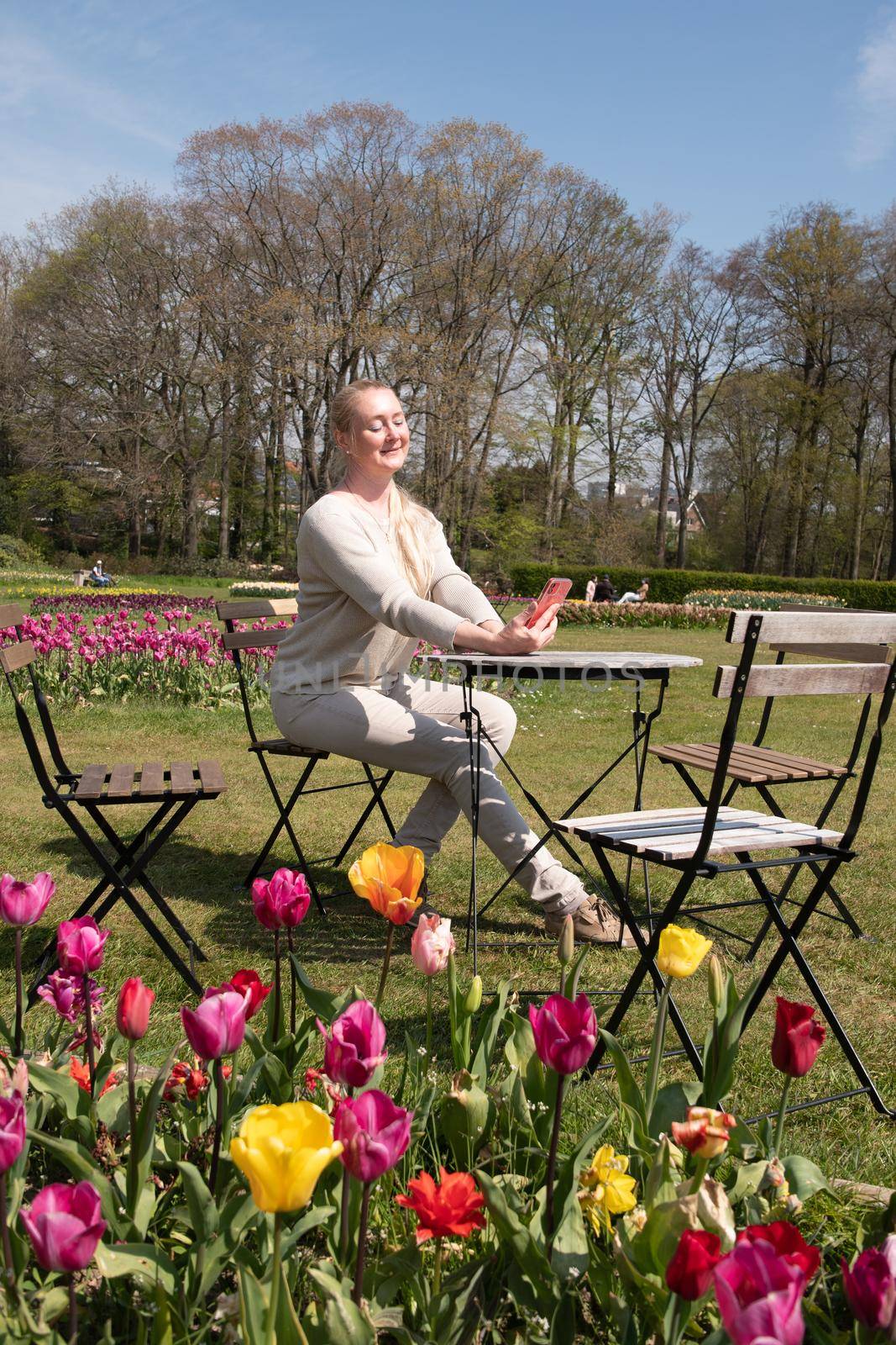 young woman in a beige jumper takes a selfie in the park with blooming tulips. High quality photo