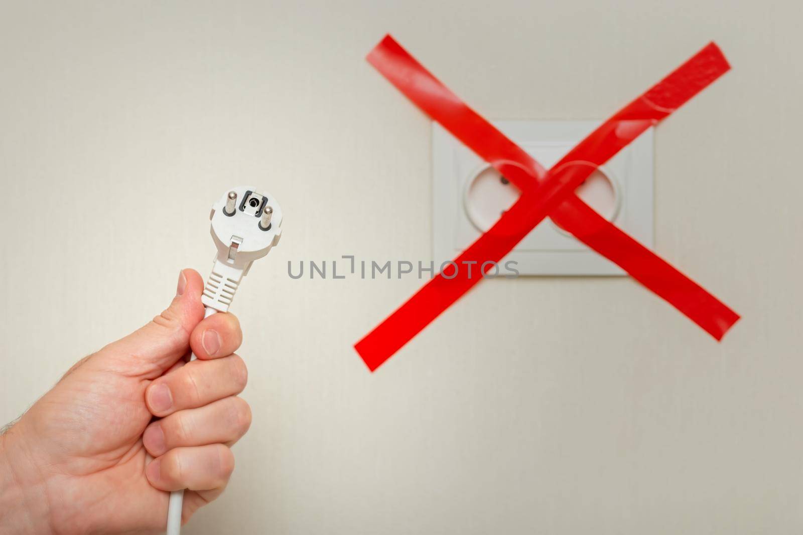 A mans hand holds a white cord with a plug near an electrical outlet, tied with a red ribbon crosswise. The concept of the energy crisis in Europe