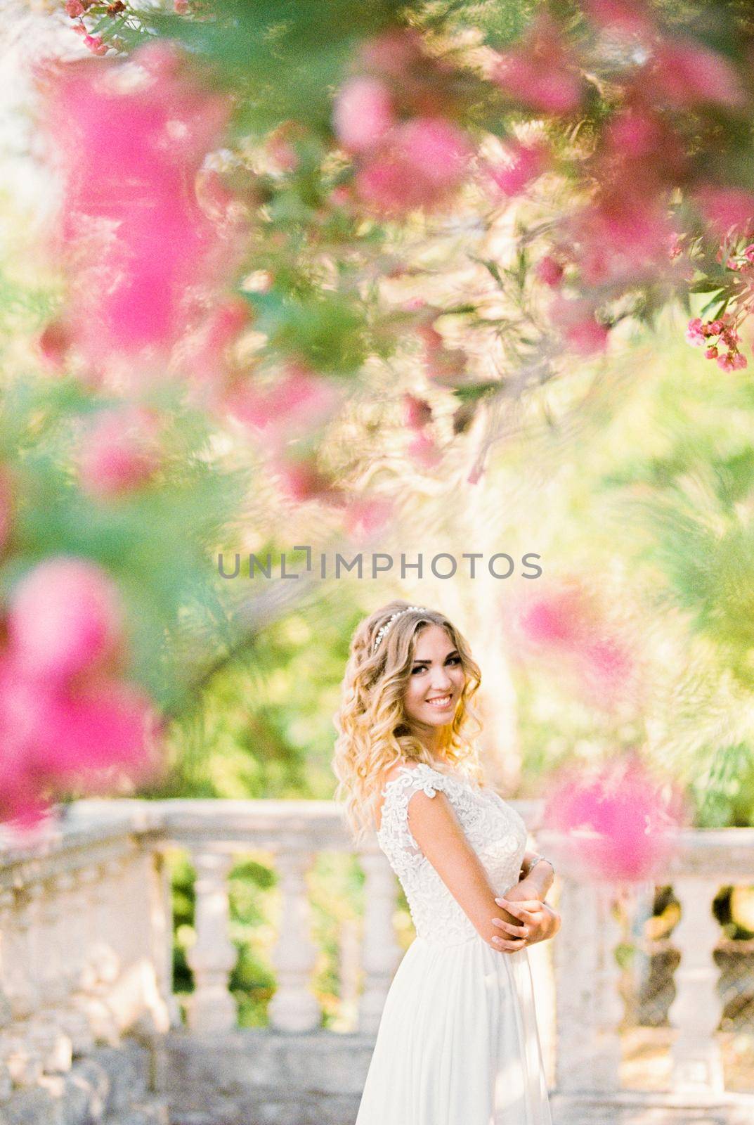 Smiling bride under a tree blooming with pink flowers in the garden. High quality photo