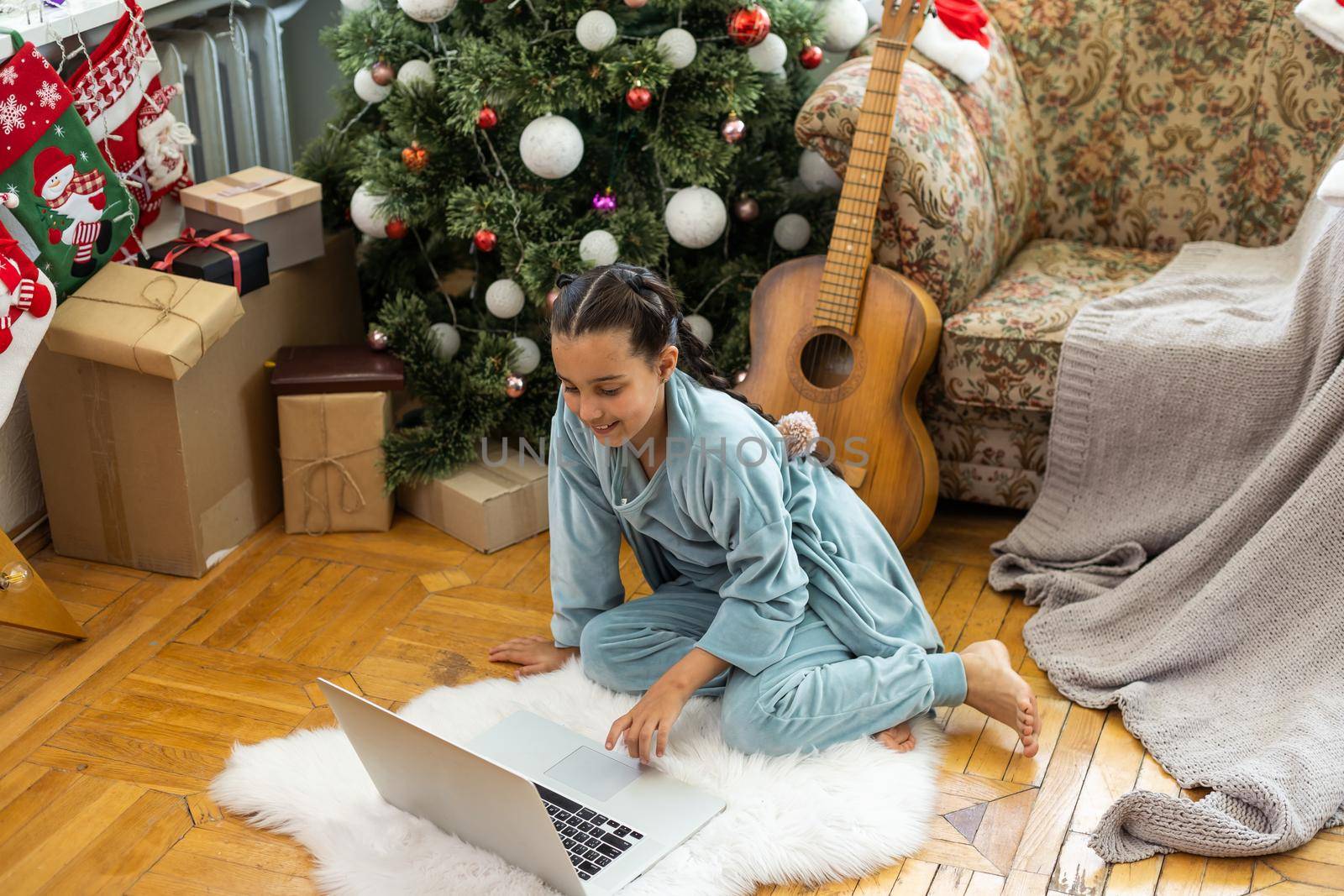 Christmas distance learning online education. Schoolgirl studying at home with laptop notebook and doing school homework by Andelov13