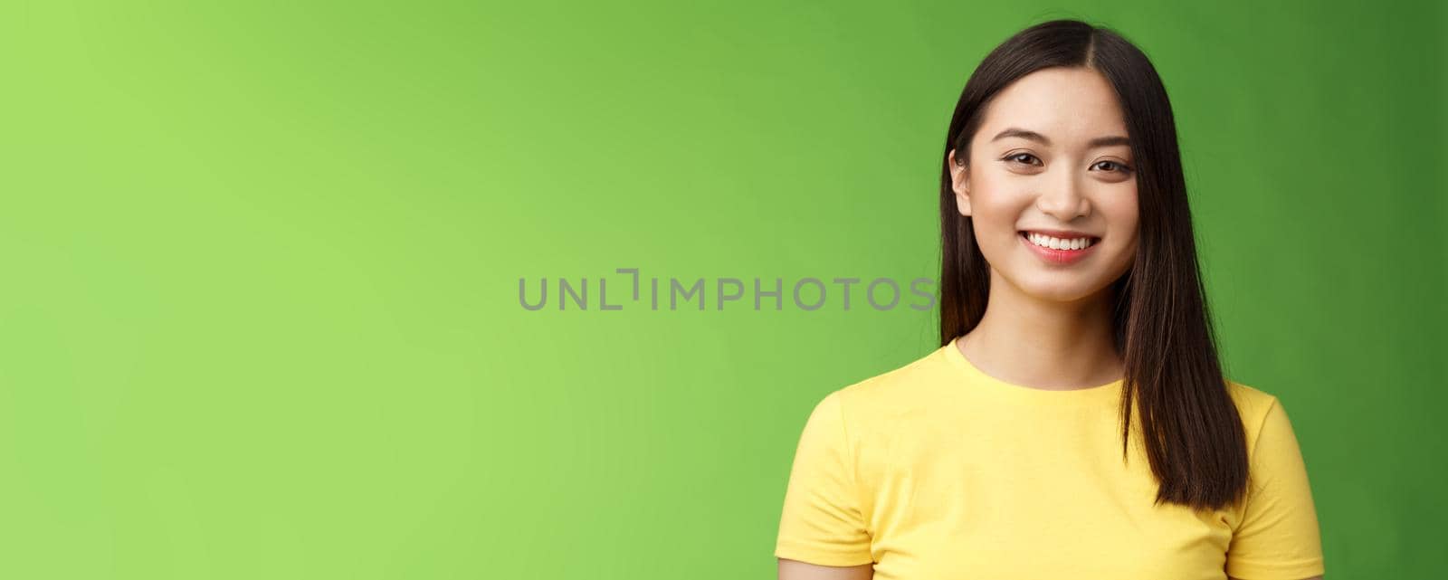 Optimistic cute carefree asian girl taking care skin condition, smiling satisfied grin happily, enjoy funny outgoing conversation, stand green background upbeat, communicate pleasantly.