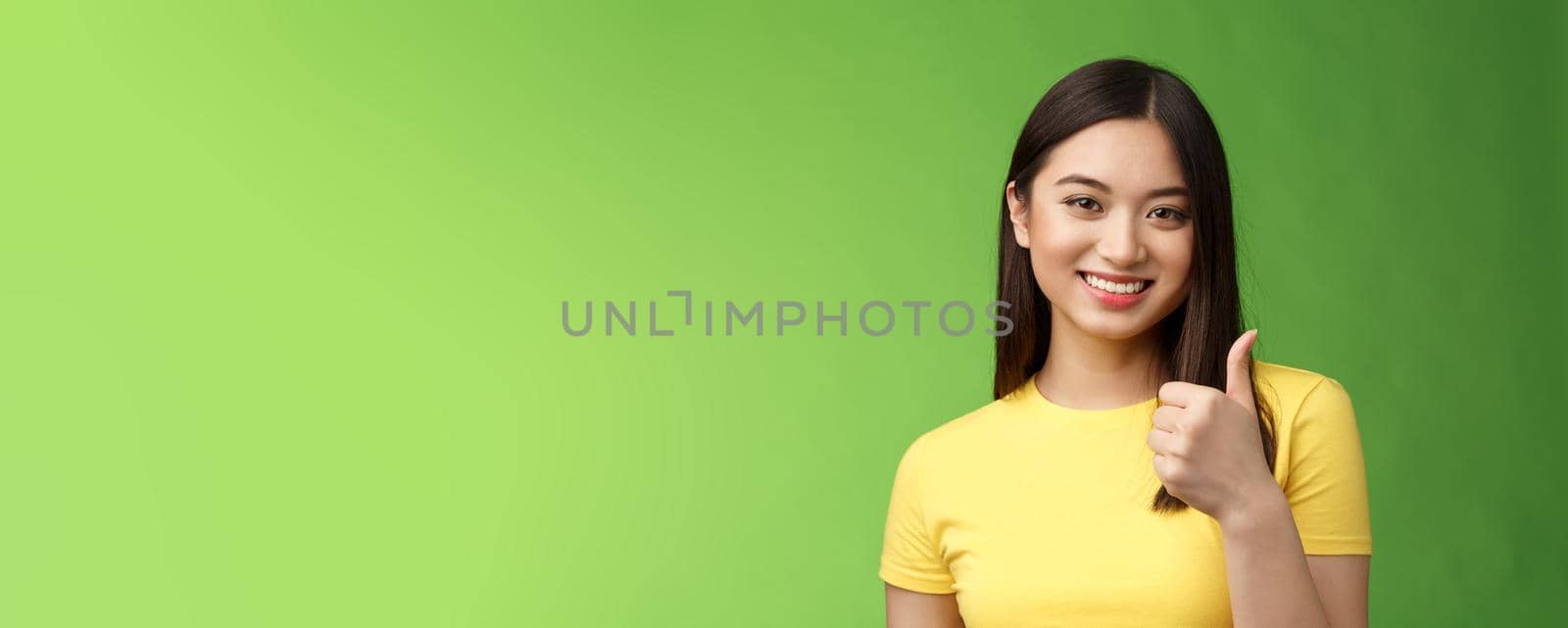 Close-up happy motivated good-looking asian woman give thumb-up smiling, approving excellent effort, like good choice, accept terms, recommend product, like idea, green background. Copy space