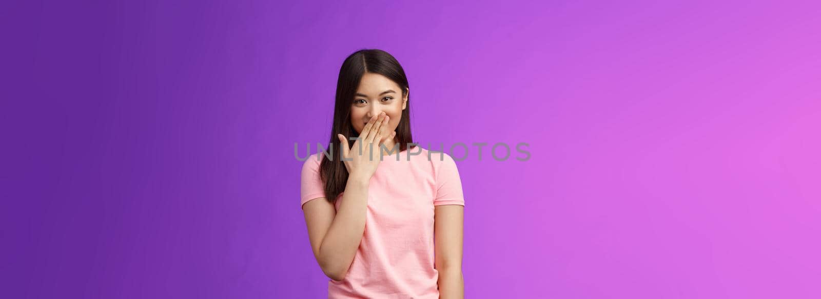 Timid cute stylish modern asian woman giggling, gossiping, cover smiling lips, laughing out loud joyfully, look camera entertained, fool around, spread funny rumors, stand purple background.