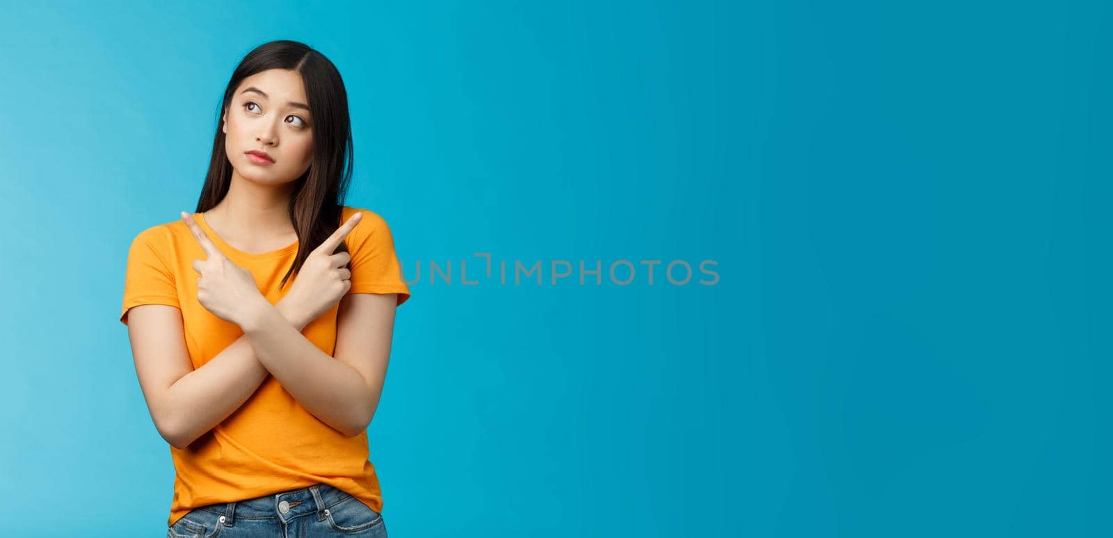 Confused cute asian female student thinking what do, look sideways thoughtful, cross hands chest pointing left and right, making choice, thinking what pick, taking important decision blue background.
