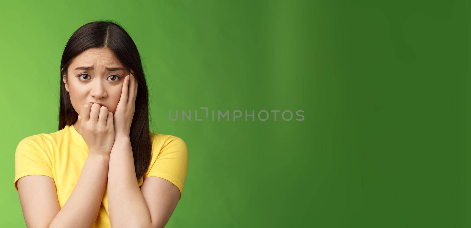Innocent insecure timid asian scared girl panicking, standing afraid victim terrified, touch cheek shocked, frowning stunned, biting fingernails, anxiously stare camera, green background by Benzoix