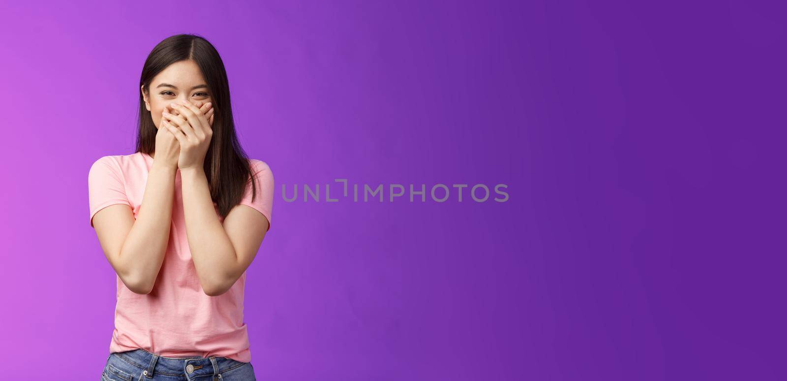 Cute carefree happy young asian girlfriend fooling around, giggle, close mouth palms not laugh loud, acting silly childish, joking, blushing receive surprising cute present, stand purple background.