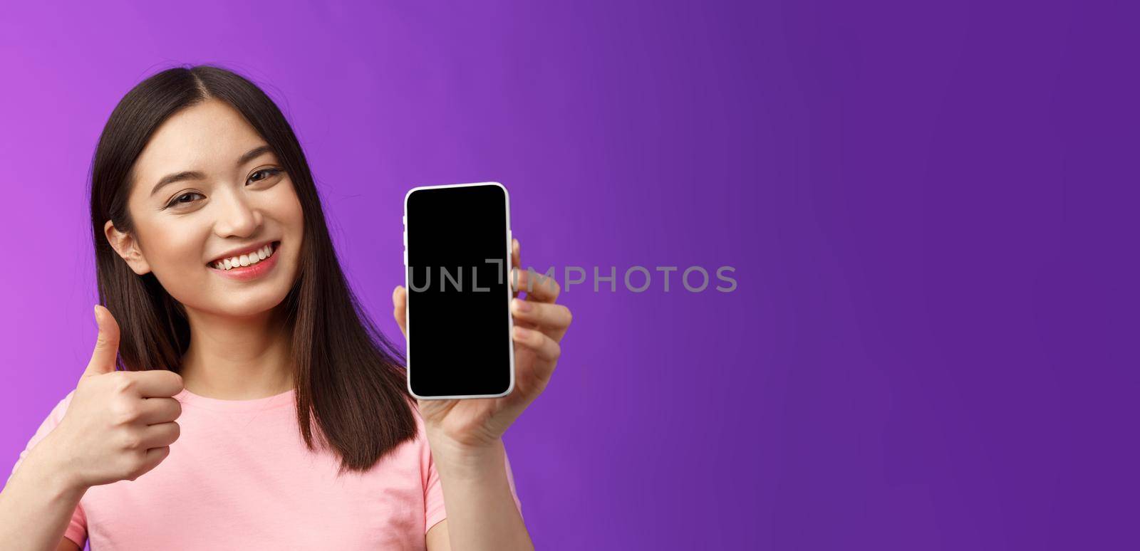 Close-up satisfied happy attractive modern asian woman give positive feedback, show smartphone display, introduce good app, raise thumb-up like application, stand purple background delighted by Benzoix