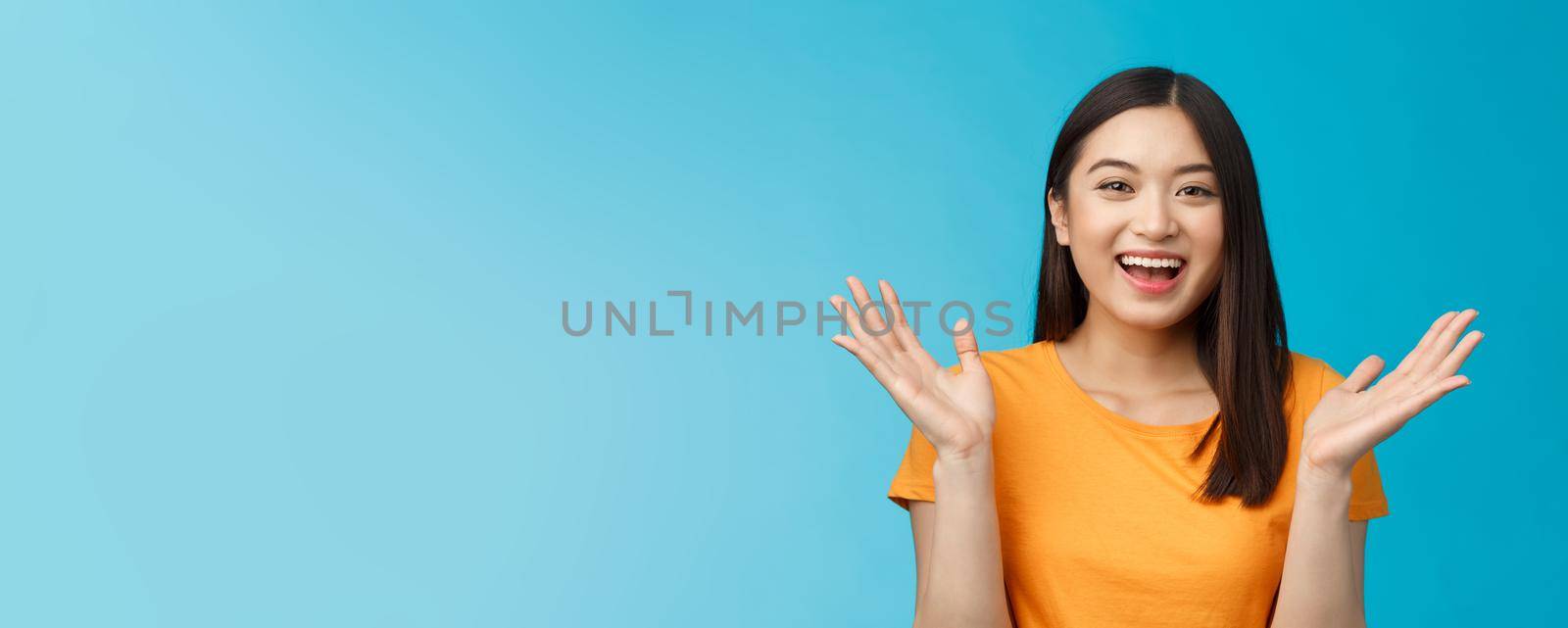Close-up friendly happy cute asian female student clap hands joyfully, smiling broadly looking funny amusing performance, stand enthusiastic blue background applause surprised. Copy space