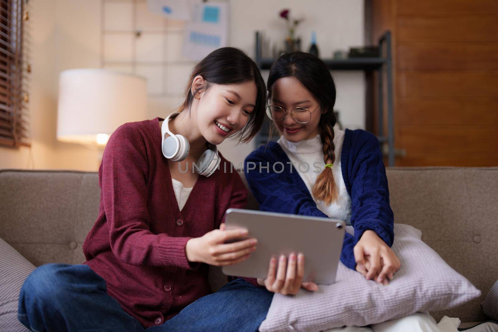 Two asian women having nice lively activity in living room on sofa in cozy interior.