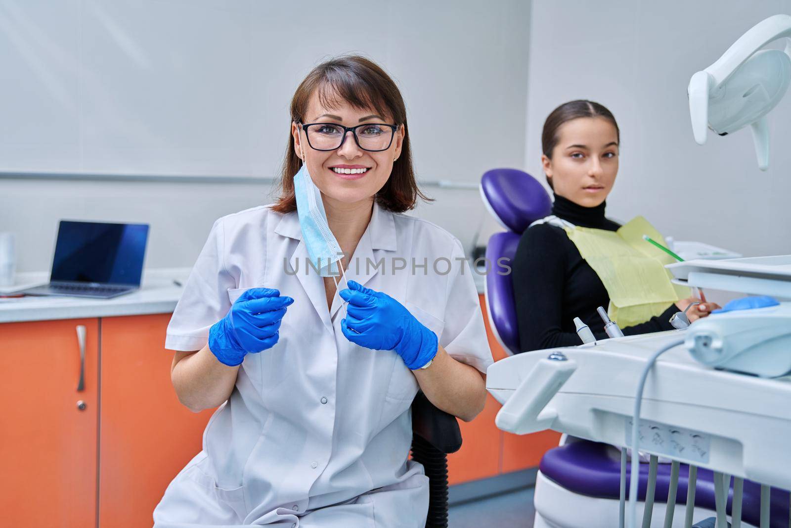 Portrait of female dentist looking at camera with young teen girl patient sitting in dental chair. Dentistry, hygiene, treatment, dental health care concept