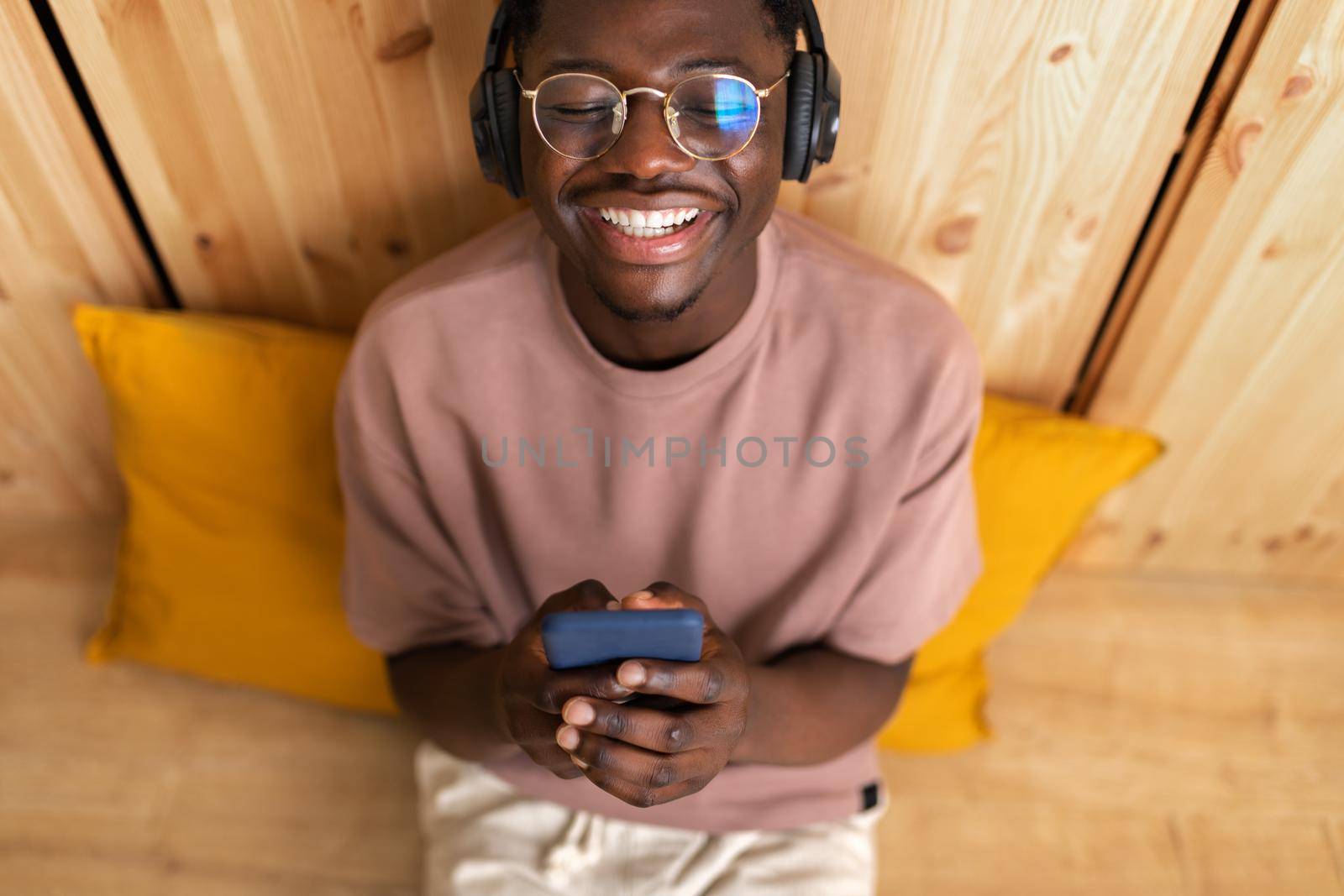 High angle view of young black man Listening to music with wireless headphones using mobile phone at home. Blissful moment. Lifestyle
