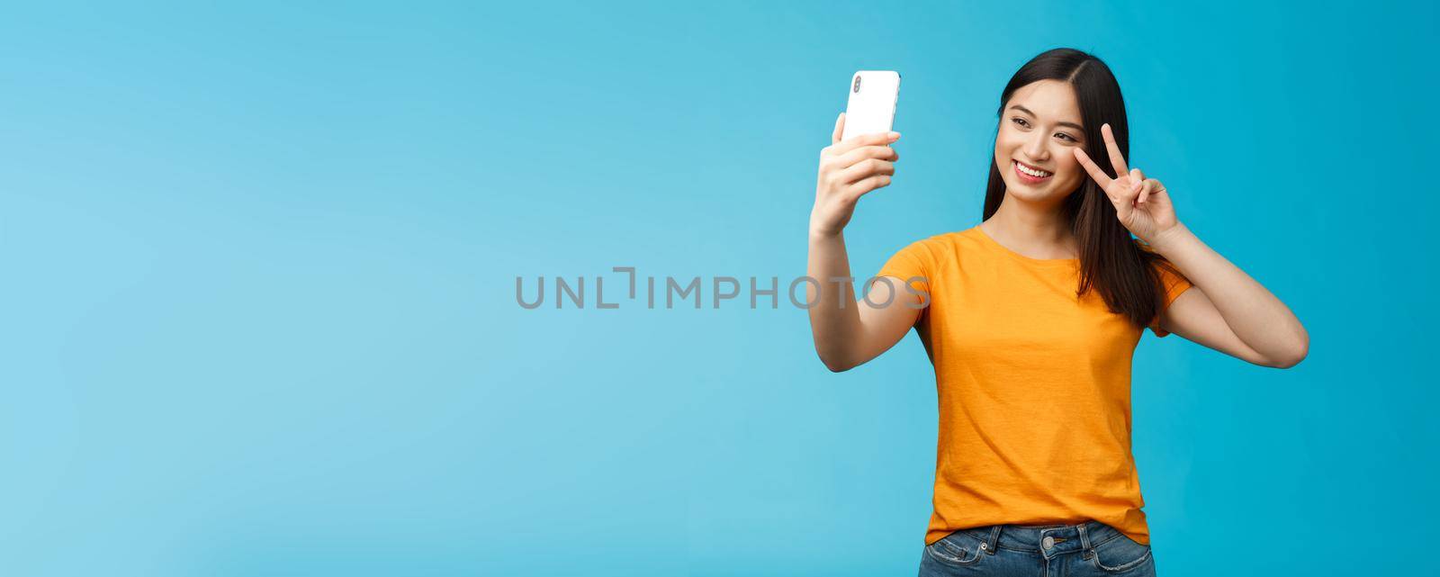 Friendly cheerful pretty asian woman brunette short haircut taking selfie, smiling joyfully hold smartphone show peace, victory sign at phone screen front camera, talking family video-call.