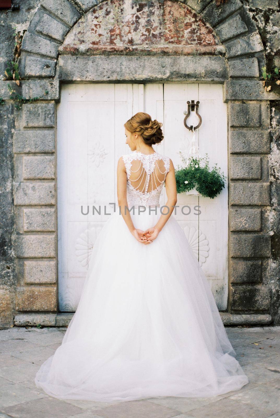 Bride stands in front of the white wooden door of an old stone building. High quality photo