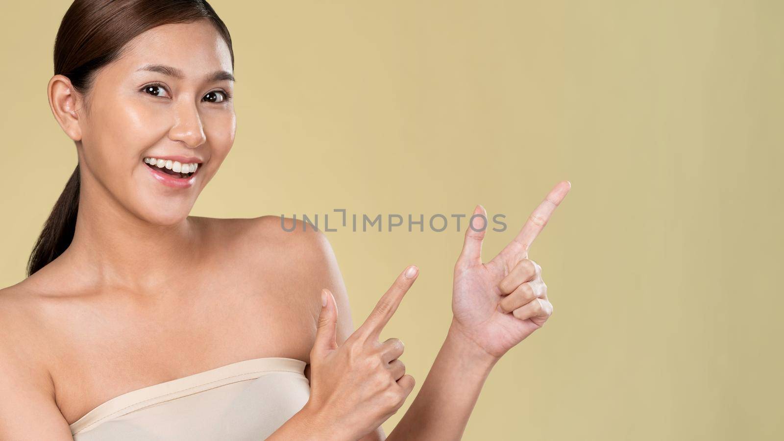 Closeup portrait of ardent woman looking at camera, finger pointing up for product, advertising text place, isolated background. Concept of healthcare advertising for skincare, beauty care product.