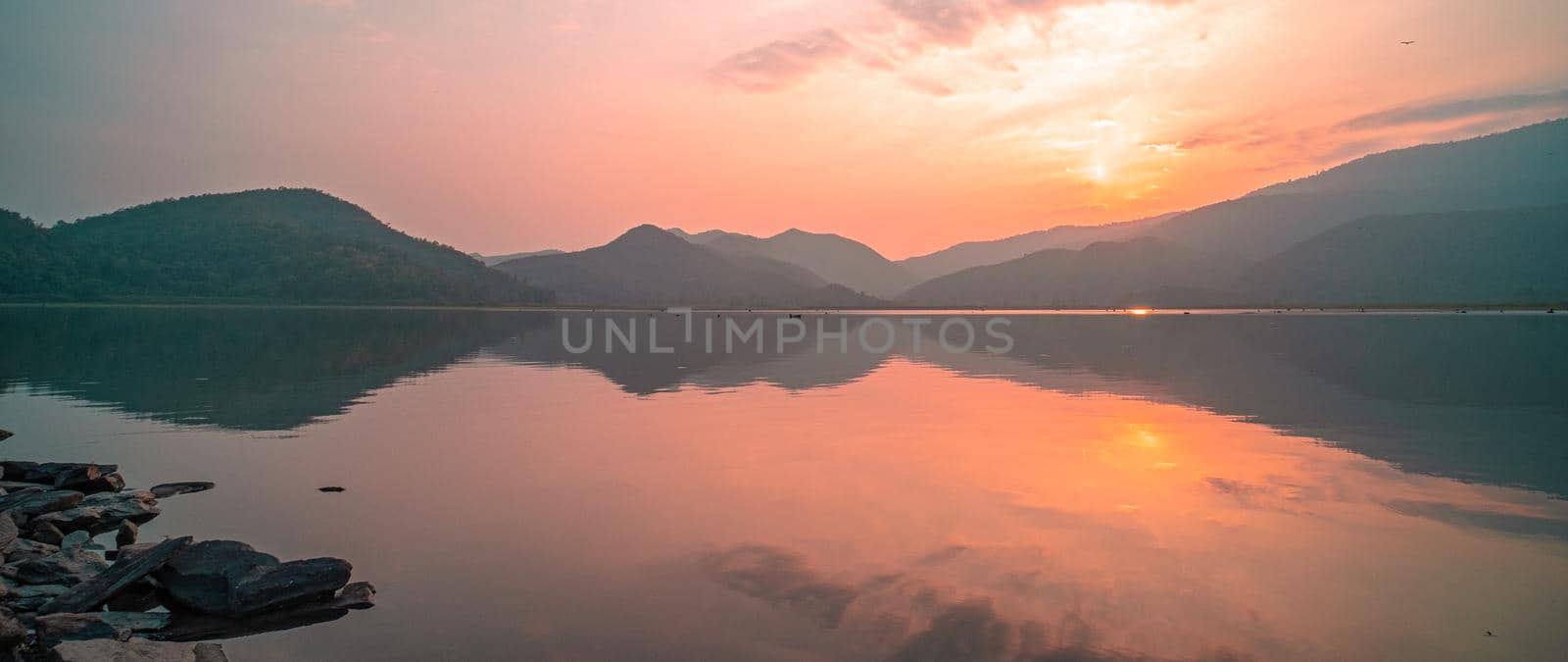 Panorama scenic of mountain lake with perfect reflection at sunrise. beautiful mountain range landscape with pink pastel sky with hills on background and reflected in water. Nature lake landscape