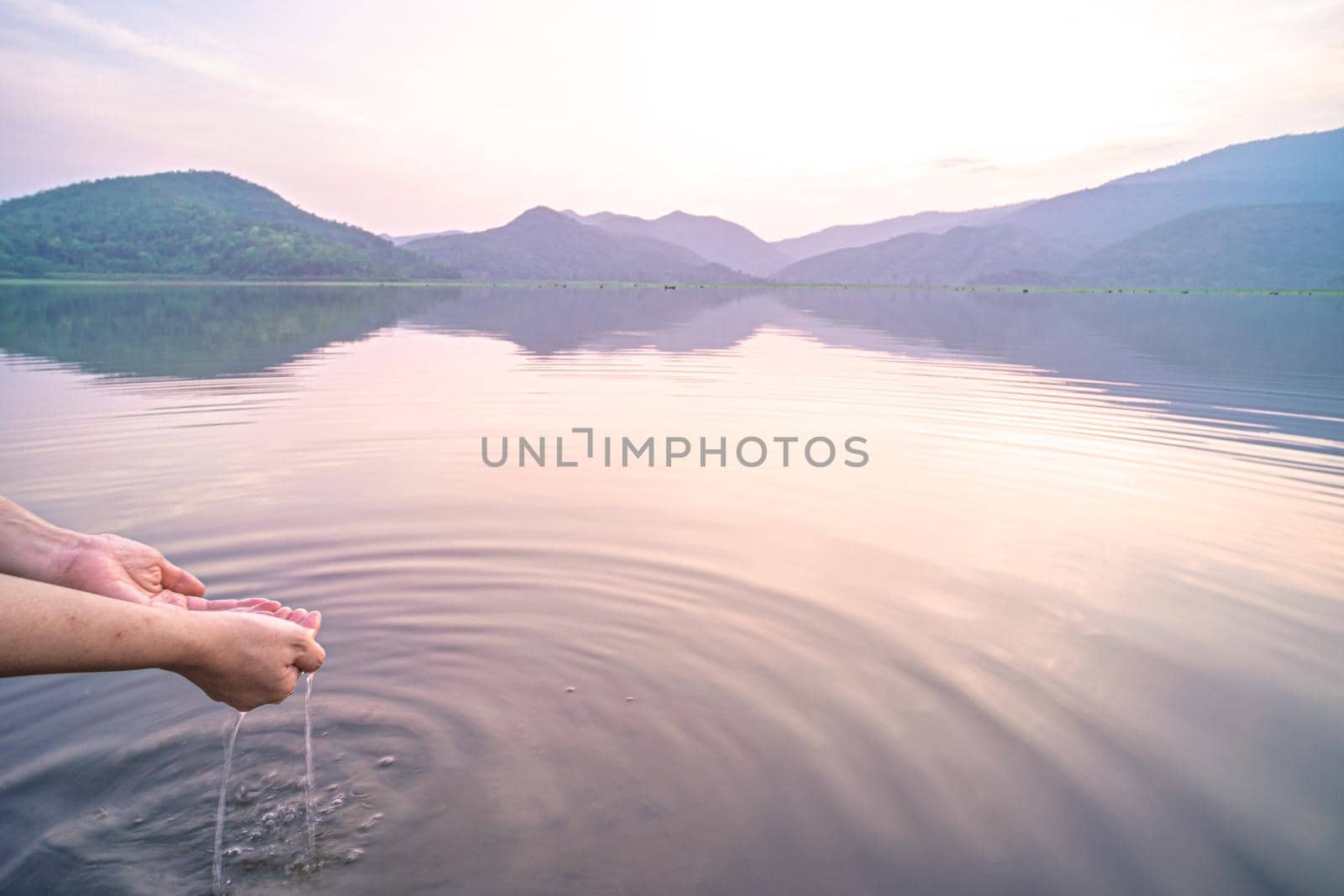 Woman taking clear water by hands on nature lake mountain background