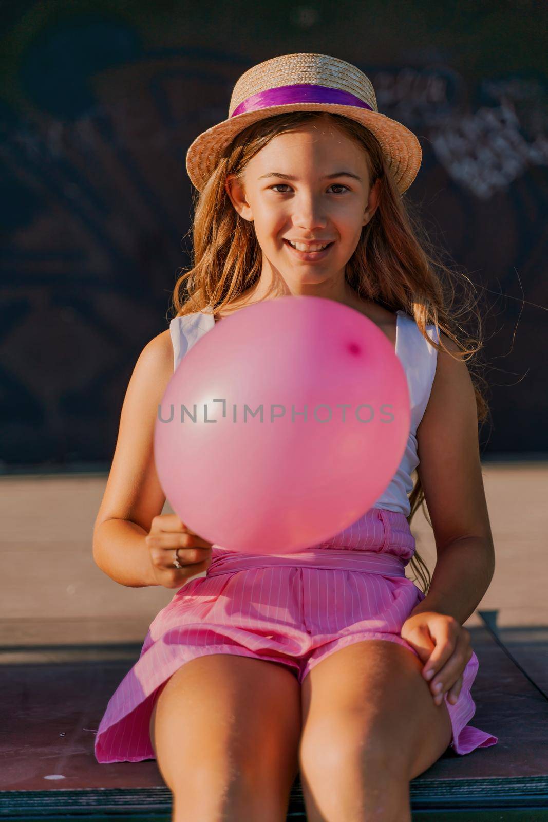 Portrait of a girl in a hat with a pink balloon. She is dressed in pink clothes and her hair is long and loose