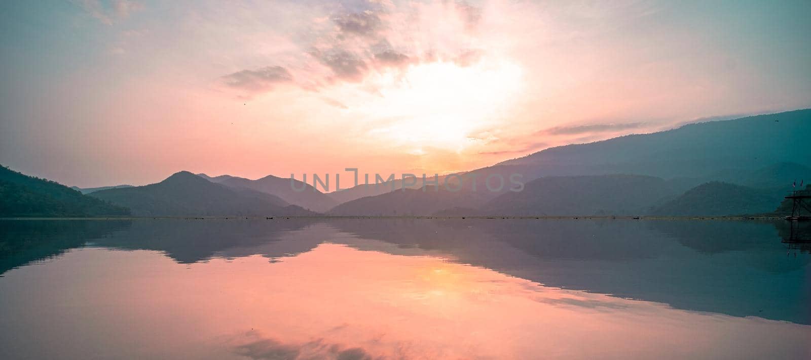 Panorama scenic of mountain lake with perfect reflection at sunrise. beautiful mountain range landscape with pink pastel sky with hills on background and reflected in water. Nature lake landscape