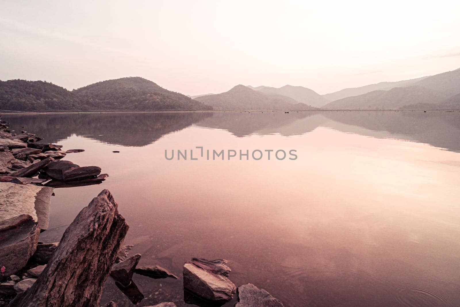Panorama scenic of mountain lake with perfect reflection at sunrise. beautiful mountain range landscape with pink pastel sky with hills on background and reflected in water. Nature lake landscape