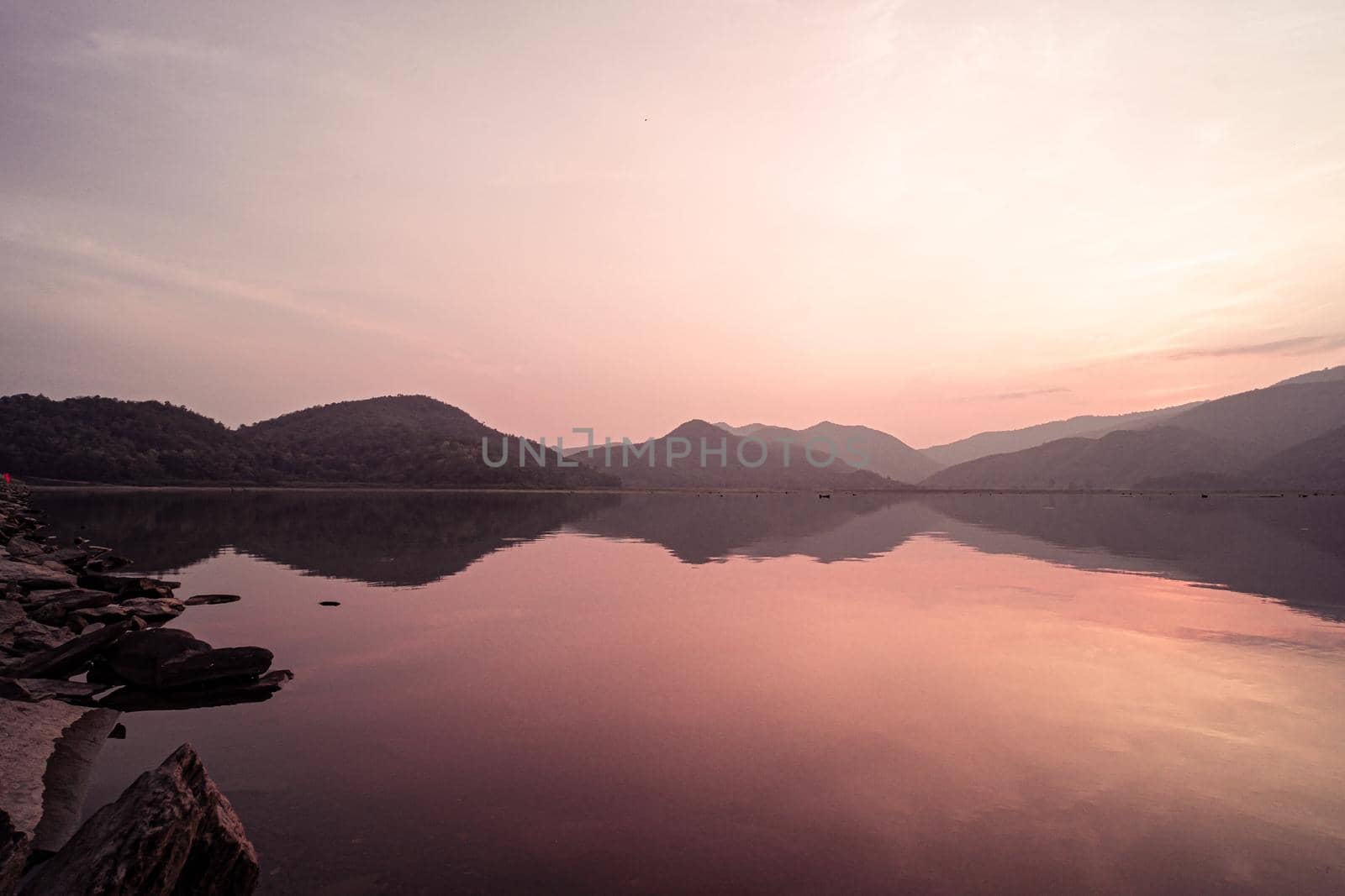 Panorama scenic of mountain lake with perfect reflection at sunrise. beautiful mountain range landscape with pink pastel sky with hills on background and reflected in water. Nature lake landscape