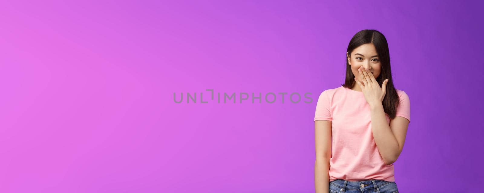Timid cute stylish modern asian woman giggling, gossiping, cover smiling lips, laughing out loud joyfully, look camera entertained, fool around, spread funny rumors, stand purple background.